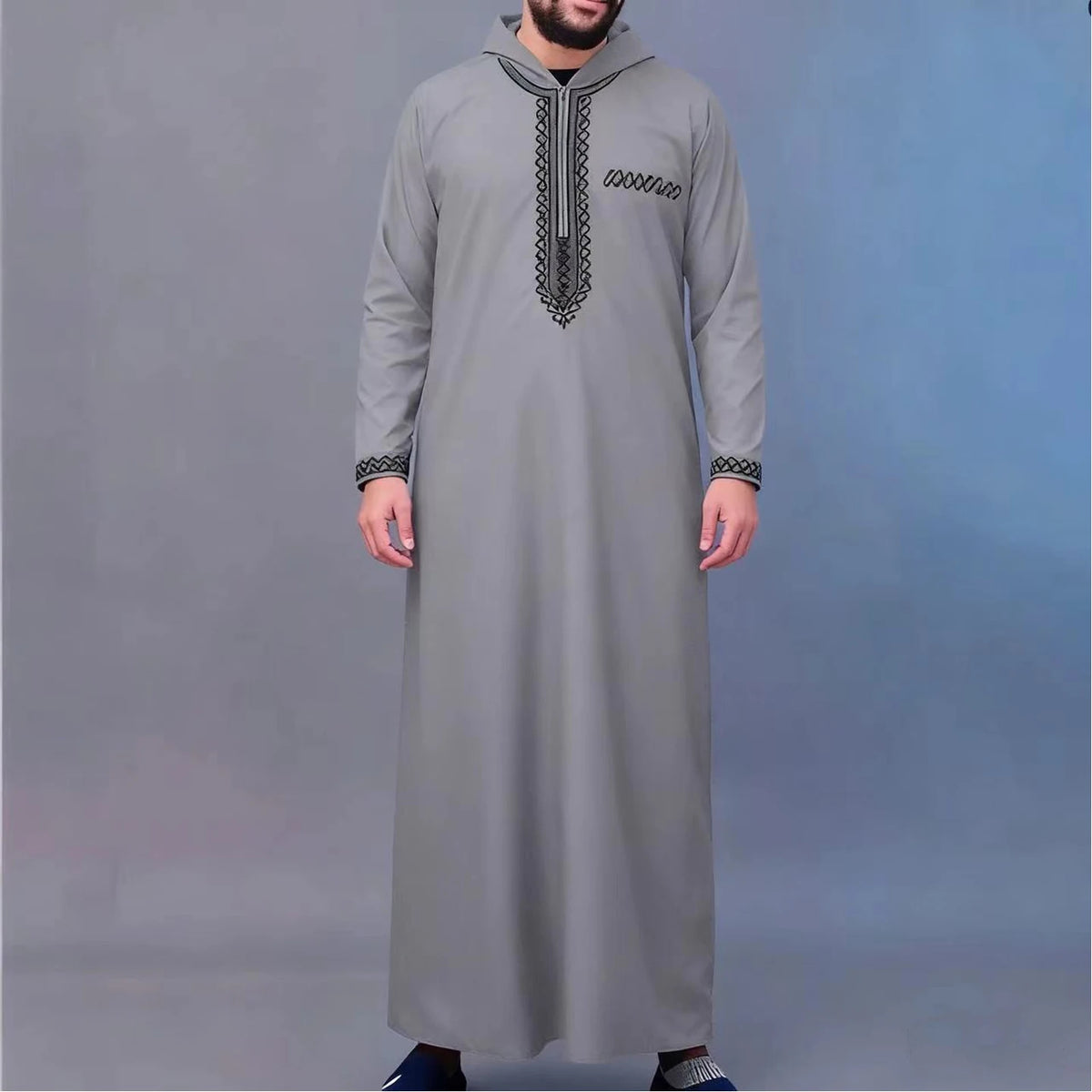 A man wearing a gray Moroccan embroidered thobe jellaba with a hood and decorative stitching.