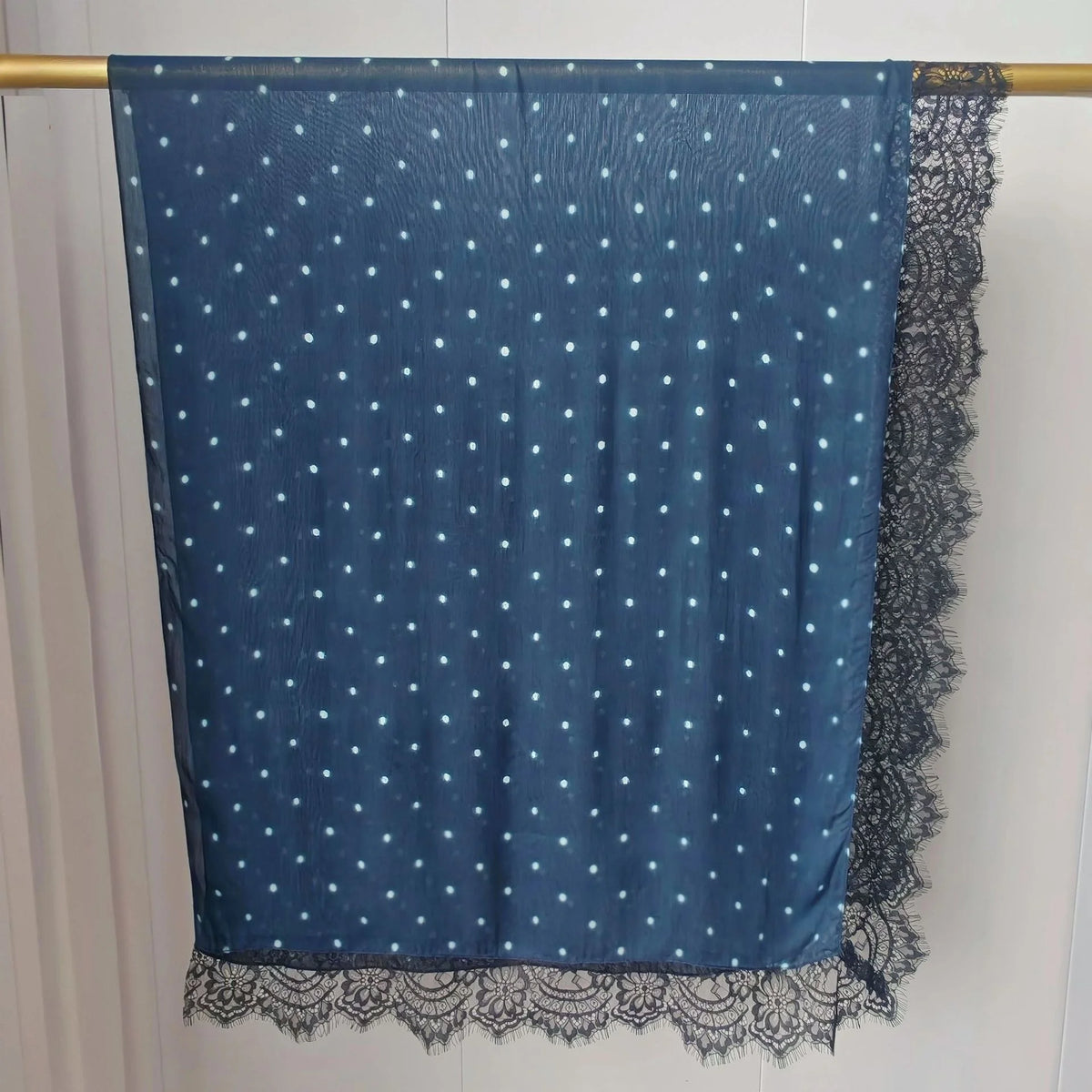 Hijab de tela transparente azul oscuro con lunares blancos y un ribete de encaje negro colgado en una barra.
