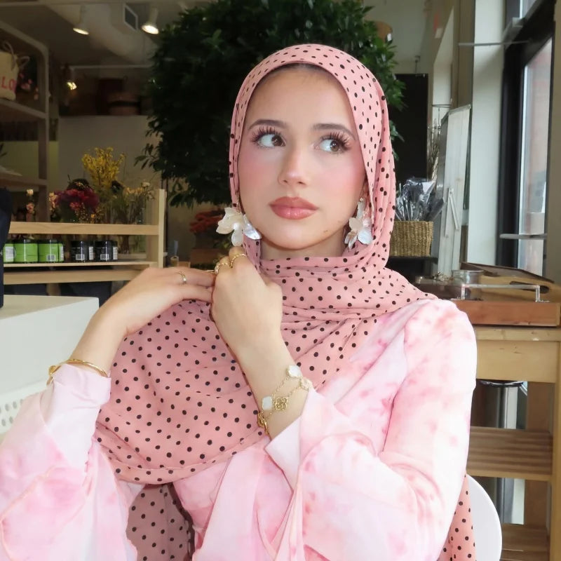 Eine Frau trägt einen rosa und schwarzen Polka-Dot-Hijab-Schal mit einem durchsichtigen rosa Oberteil.