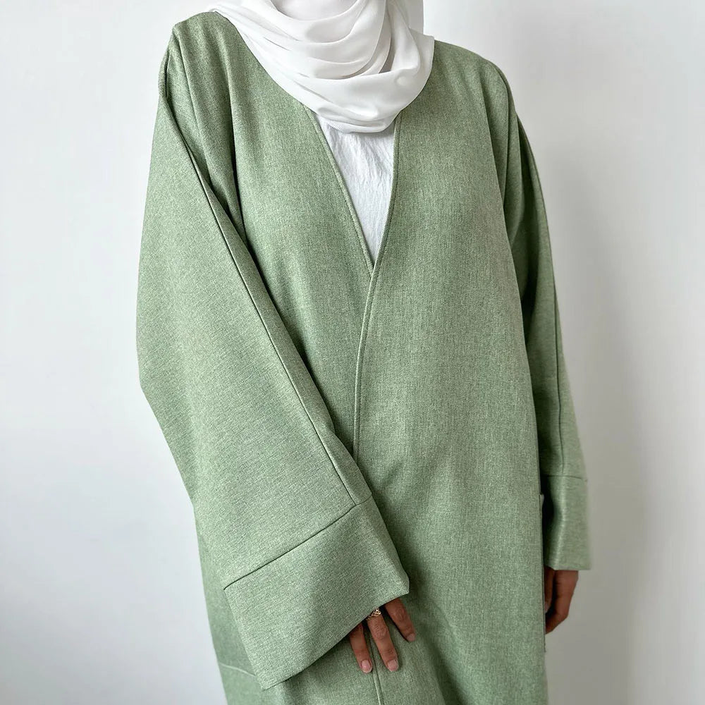 Helles salbeigrünem Leinen-Kimono-Abaya über einem weißen Oberteil und einem weißen Hijab getragen.