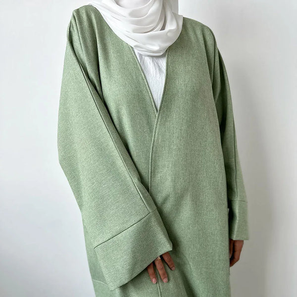 A light sage green linen kimono open abaya worn over a white top and a white hijab.