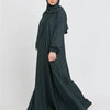 Eine Frau in einem dunkelgrünen marokkanischen Kaftan-Abaya mit Hijab vor hellem Hintergrund.