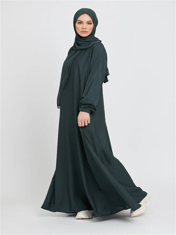 Eine Frau in einem dunkelgrünen marokkanischen Kaftan-Abaya mit Hijab vor hellem Hintergrund.