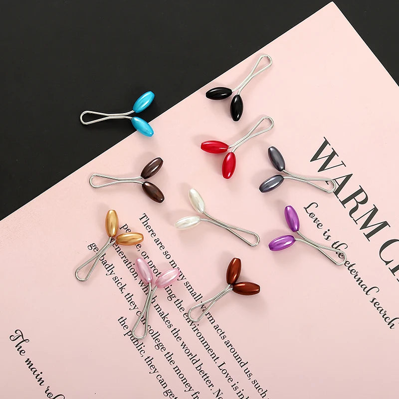 A collection of twelve pearl-colored brooch headscarf pins arranged on a pink surface.