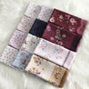 Eine Sammlung von neun floralen quadratischen Hijab-Schals in verschiedenen Mauve-, Violett- und Pinktönen auf weißem Pelz.