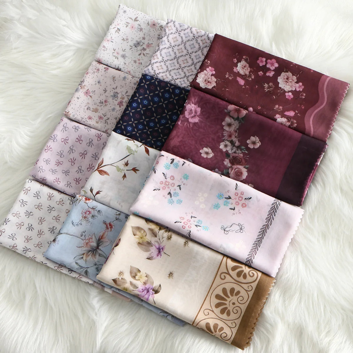 Eine Sammlung von neun floralen quadratischen Hijab-Schals in verschiedenen Mauve-, Violett- und Pinktönen auf weißem Pelz.