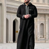 A man wearing a black Moroccan ethnic thobe with a stand collar and silver embroidery.