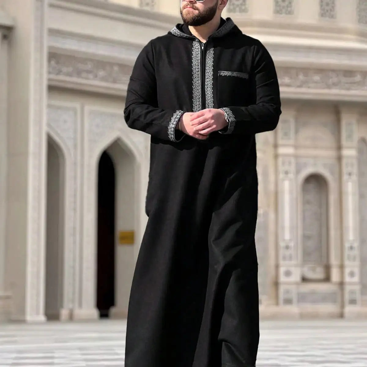 A man wearing a black Moroccan ethnic thobe with a stand collar and silver embroidery.