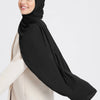 A woman wearing a black chiffon hijab and a beige outer garment.