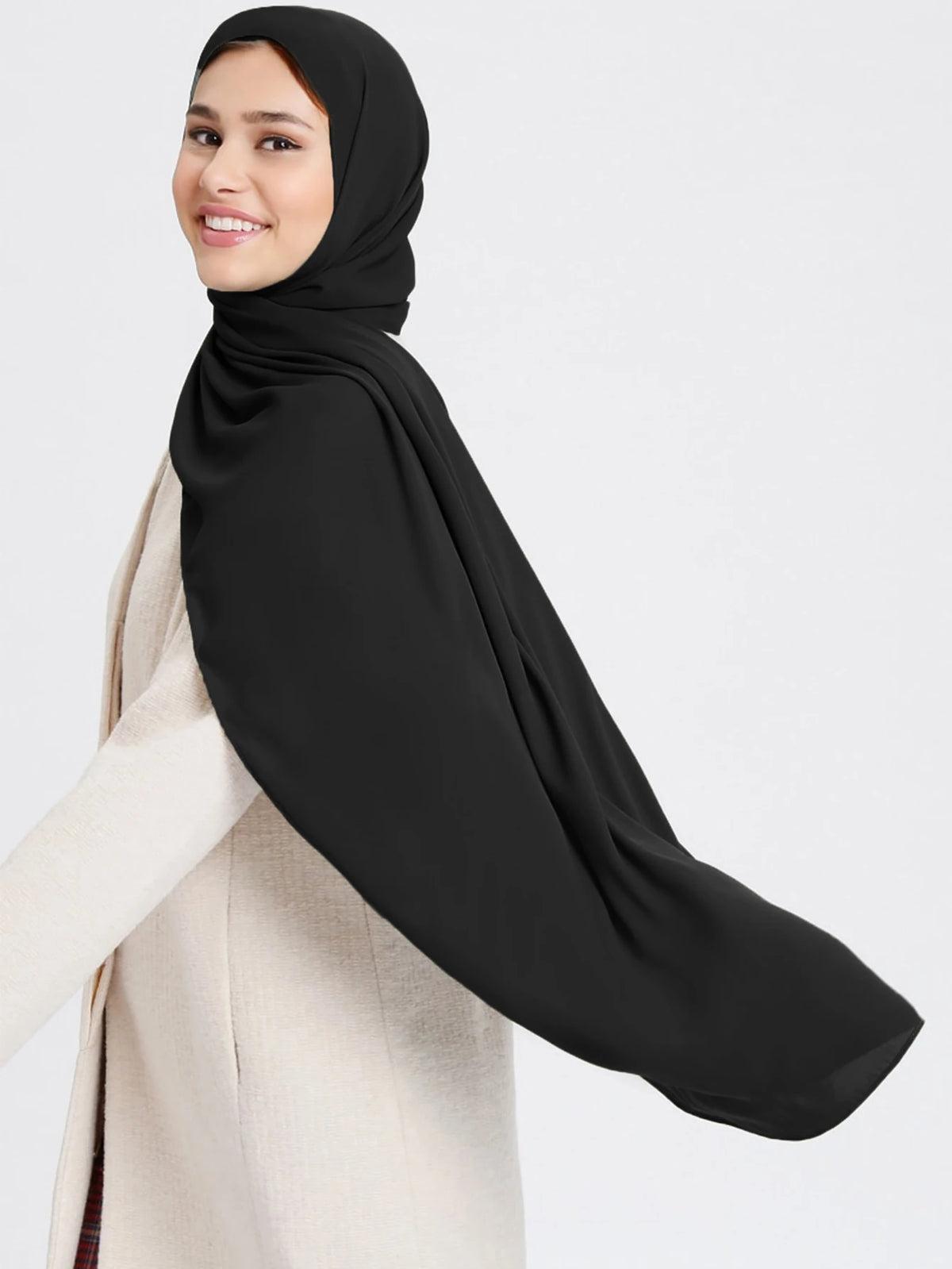 A woman wearing a black chiffon hijab and a beige outer garment.