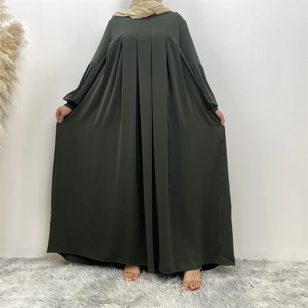 Eine Frau trägt ein elegantes, langes, dunkel olivgrünes islamisches Kleid mit voluminösen Ärmeln und einem vollen Rock.