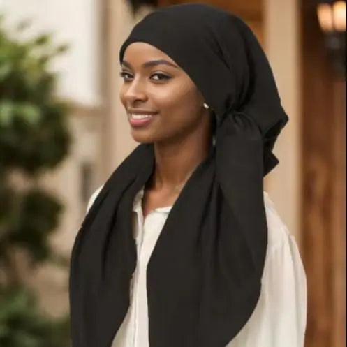 Una mujer vistiendo un hiyab negro y una blusa blanca, mirando hacia adelante.