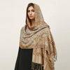 Una mujer vistiendo un pañuelo pashmina de lujo con estampado beige y dorado sobre su hombro.