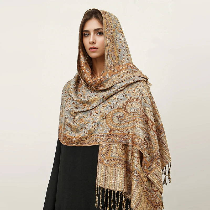 Una mujer vistiendo un pañuelo pashmina de lujo con estampado beige y dorado sobre su hombro.
