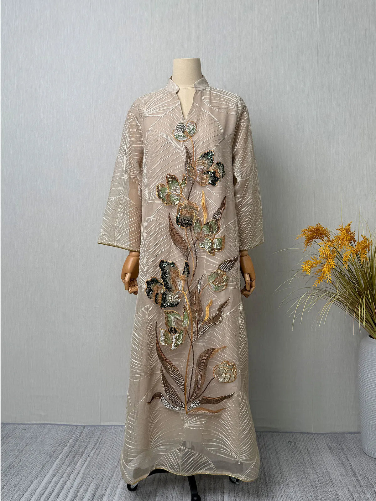 Beige, durchscheinende Abaya mit goldenen und silbernen Pailletten-Blumenmustern auf einem Mannequin.