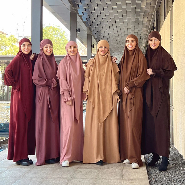Five women wearing elegant brown and mauve abayas and khimars standing in a modern hallway.