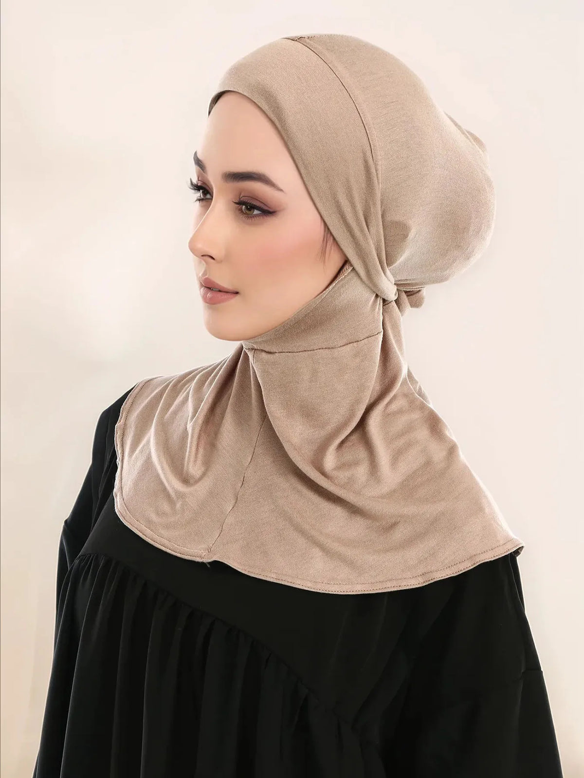 Una mujer vistiendo un hiyab beige de cobertura completa con un lazo sobre una blusa negra.