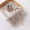 Un châle crinklé, léger et scintillant beige, drapé dans un cadre en bois.
