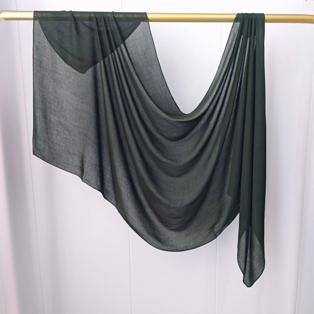 Un foulard modal gris foncé transparent drapé sur un cintre en bois.