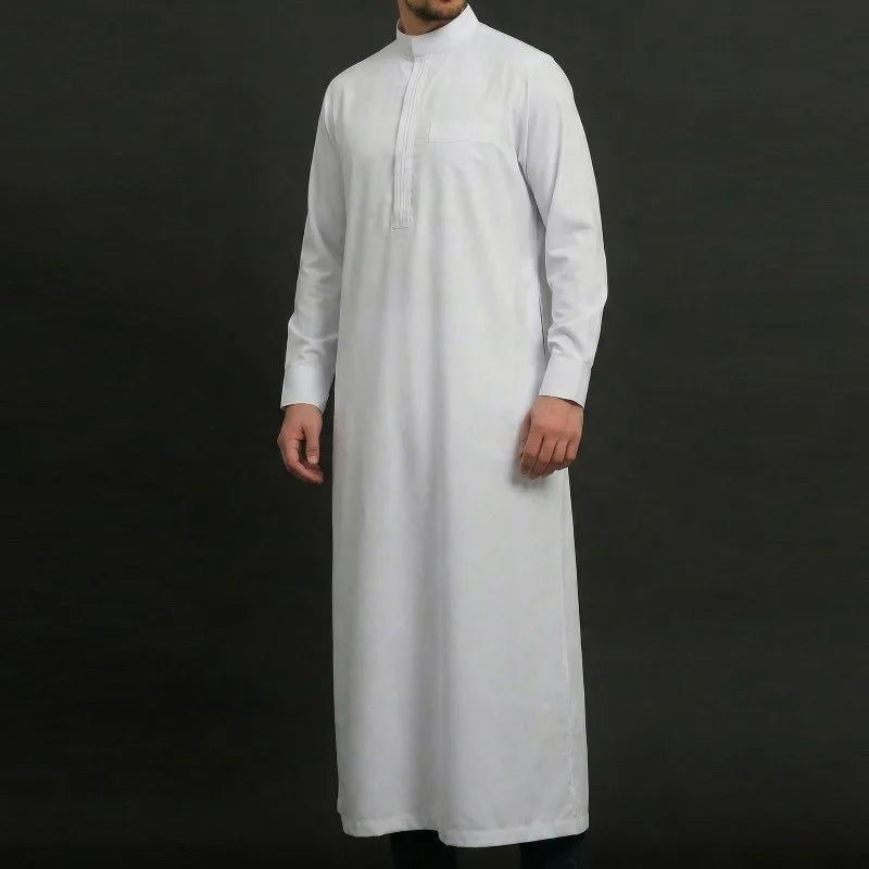 Un hombre vistiendo una jubba thobe bordada blanca, bata casual contra un fondo oscuro.