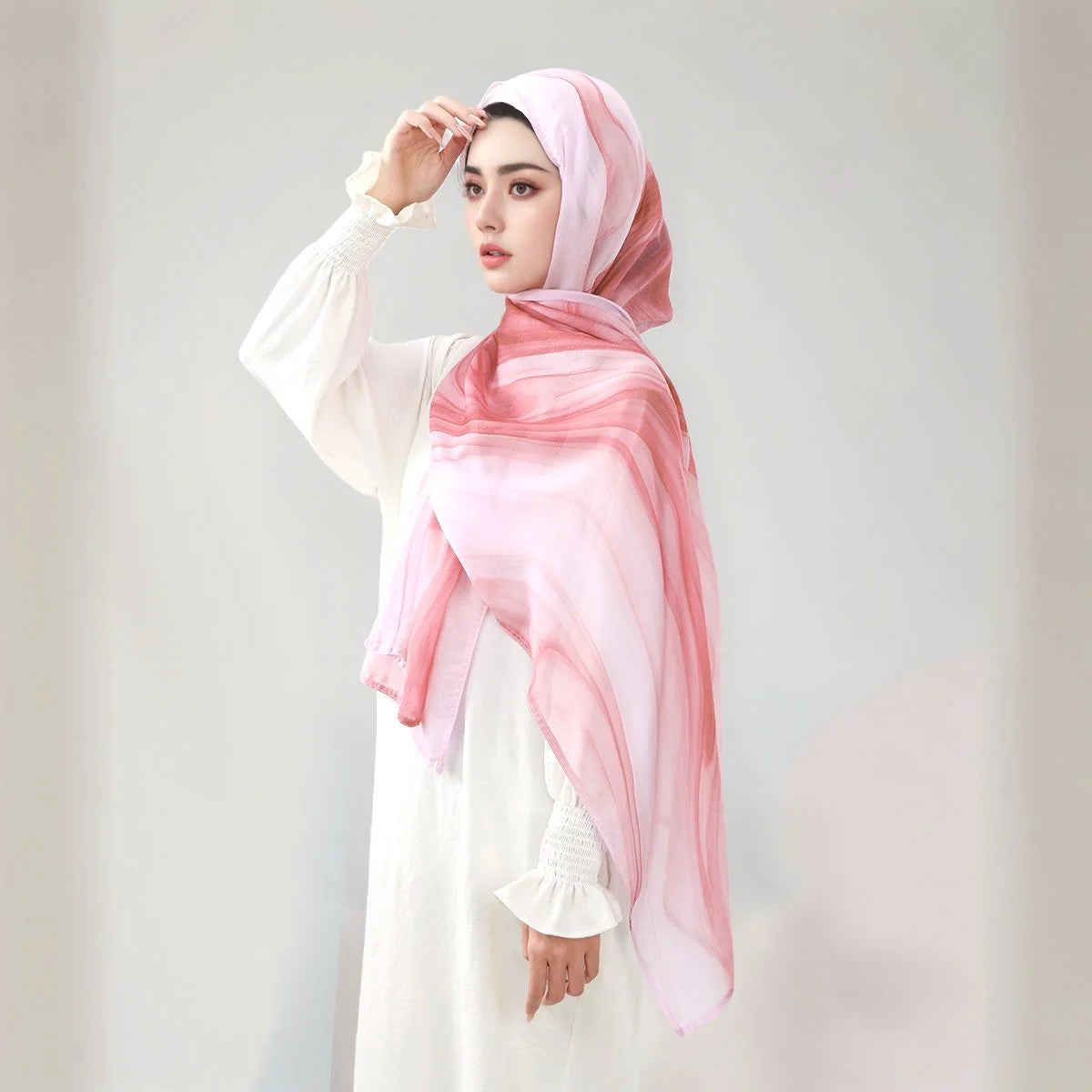 Eine Frau trägt einen rosa-weißen Aquarelldruck-Baumwoll-Leinen-Hijab-Schal mit einem weißen Langshirt.