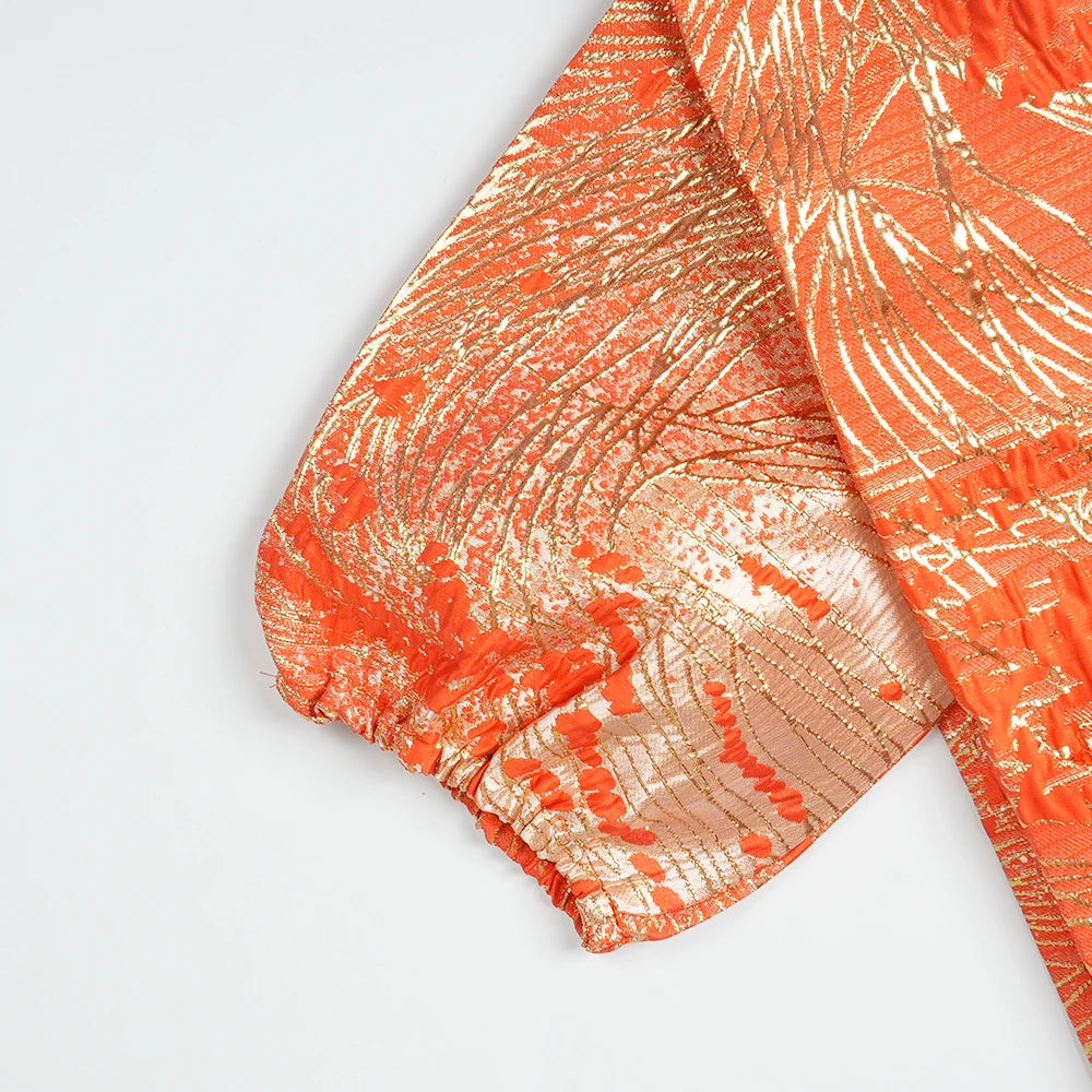 Close-up of an orange satin kaftan fabric with a subtle gold pattern and gathered cuff detail.