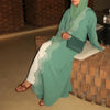 Una mujer vistiendo un elegante vestido kaftan maxi verde menta con ribetes blancos y un hiyab a juego, sentada sobre una sup