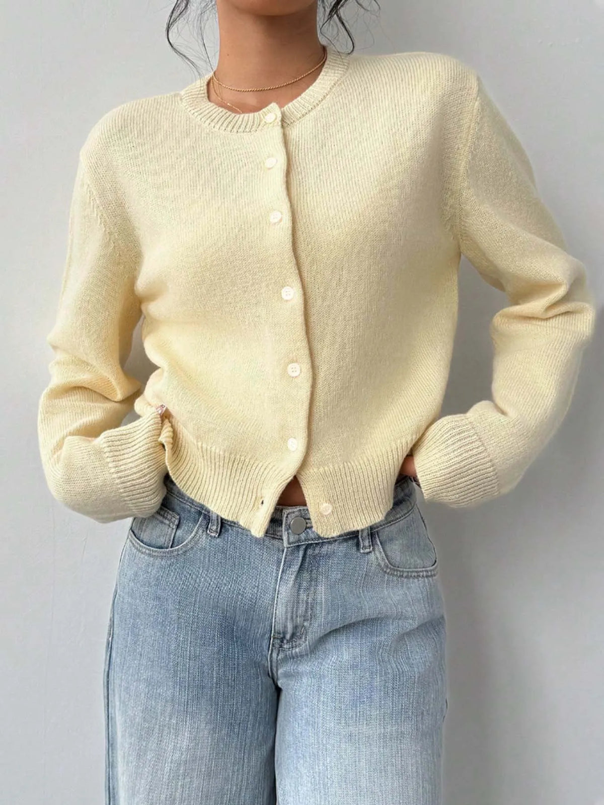 Une femme porte un pull en tricot jaune pâle sur un jean clair délavé.