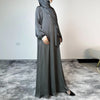 Una mujer vistiendo un largo y fluido vestido abaya maxi de satén gris y hijab, de pie en interiores.