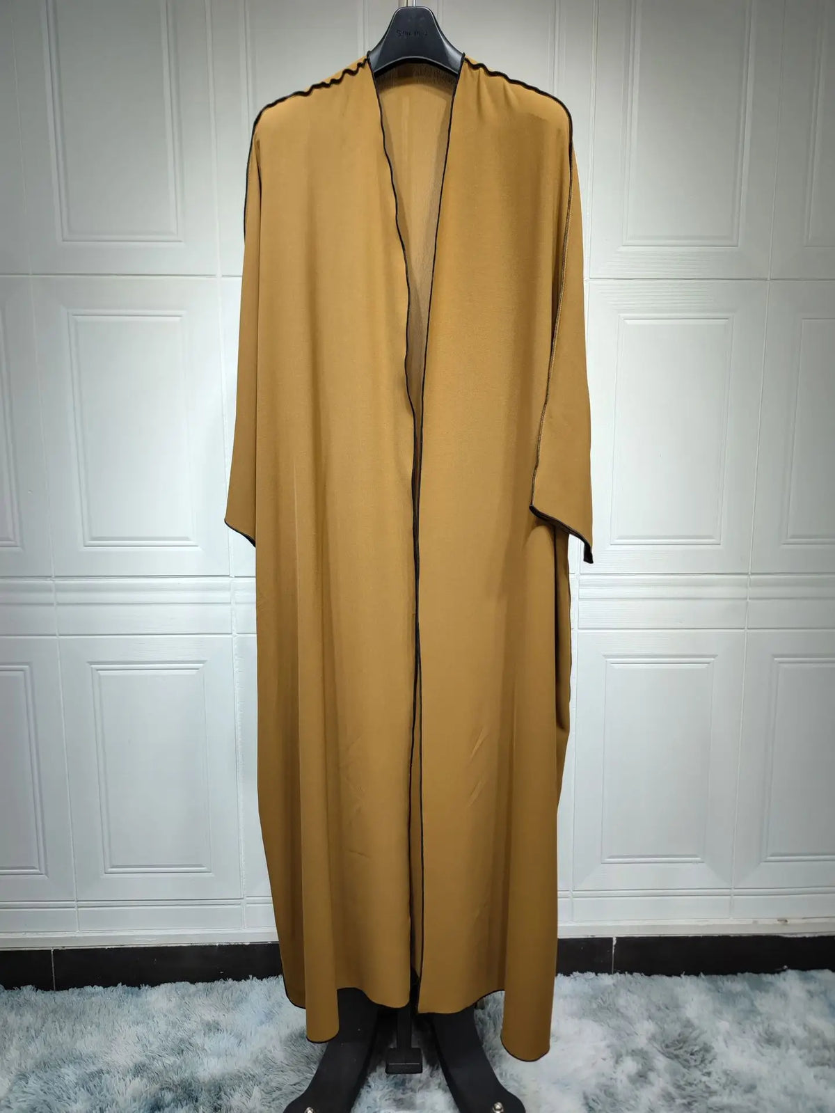 Vestido abaya oversize color marrón oliva completo, exhibido en percha contra pared blanca con paneles.