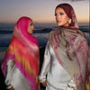 Une femme portant un élégant foulard voile imprimé rose et violet, avec un arrière-plan de coucher de soleil.