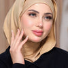 Eine Frau trägt einen beige-Instant-Jersey-Hijab und ein schwarzes Oberteil und blickt in die Kamera.