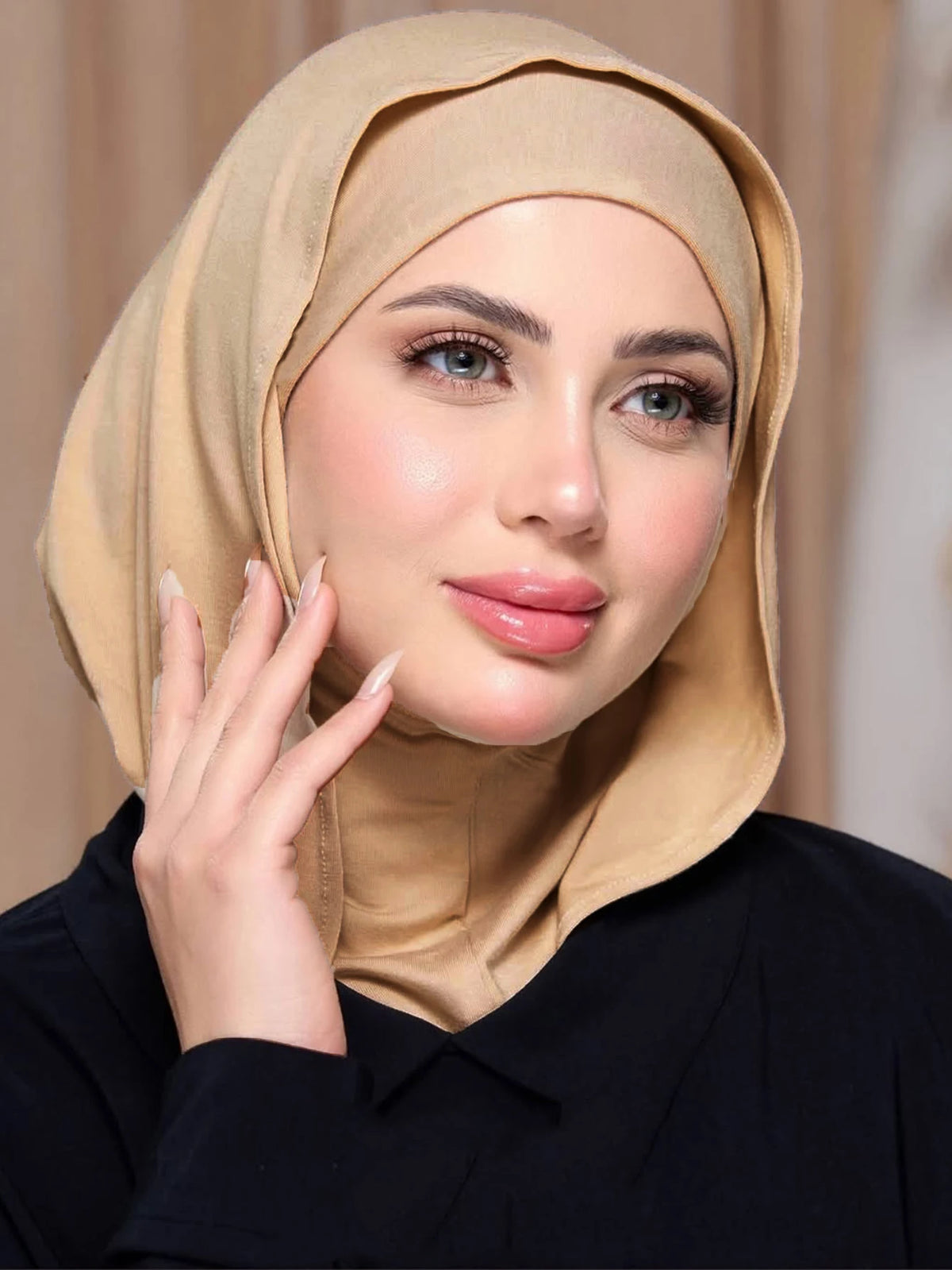 Eine Frau trägt einen beige-Instant-Jersey-Hijab und ein schwarzes Oberteil und blickt in die Kamera.
