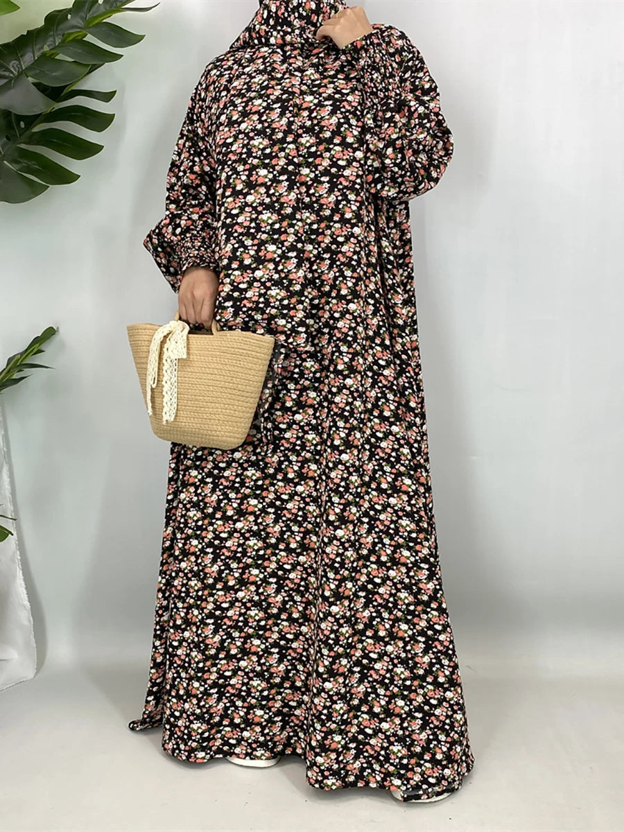 Una mujer vistiendo una elegante caftán de abaya floral con mangas largas y un vestido estampado, sosteniendo una bolsa tejid