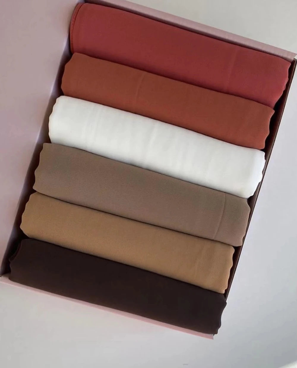 Ein Set von sechs Chiffon-Hijab-Schals in verschiedenen Rosa-, Beige- und Weißtönen in einer Box.