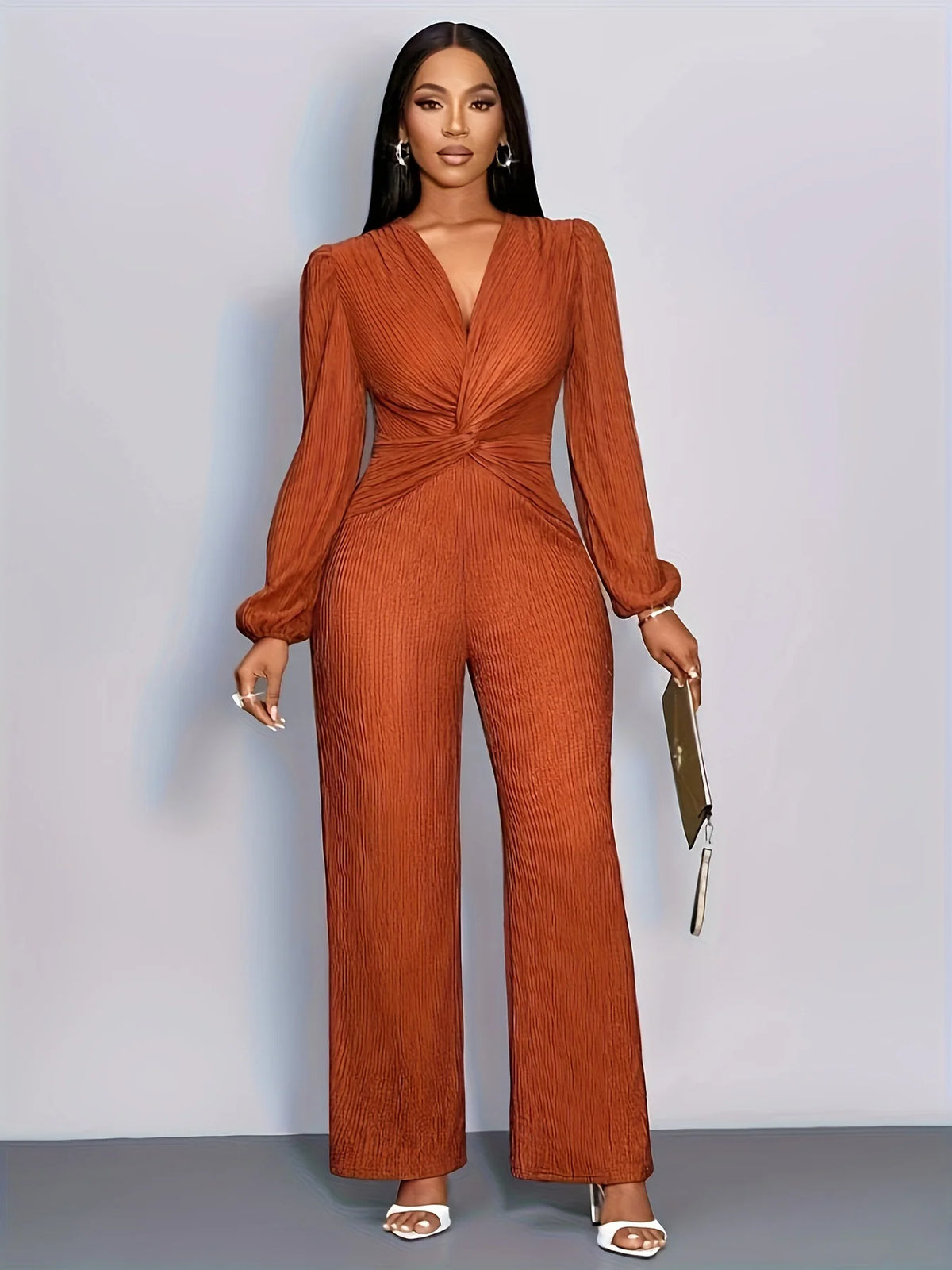 A woman models an orange ribbed knit jumpsuit with a deep V-neck and puff sleeves.