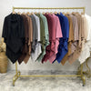 A rack of two-layer everyday hijab scarves in various muted and deep colors displayed on a gold hanger.
