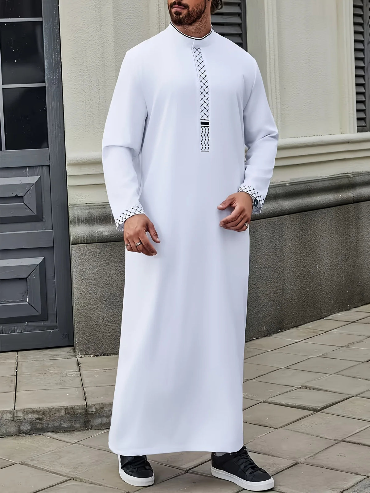Mann in weiß besticktem Jubba Kaftan mit schwarzen Sneakern im Freien