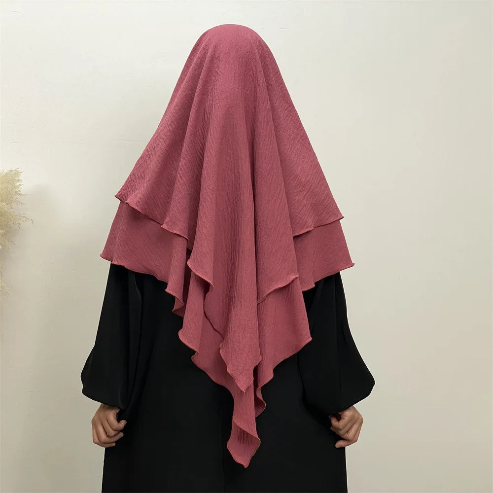 A woman wearing a dusty rose two-layer everyday hijab scarf over a black garment.