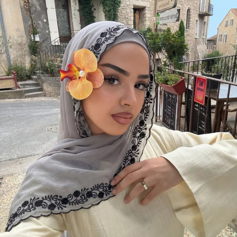 Une femme portant un hijab de mousseline gris doux avec des détails en dentelle noire et un haut jaune pâle, posant à l'extér