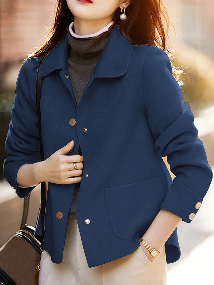 Une femme portant un manteau en laine bleu marine sur un col roulé gris et un pantalon clair.