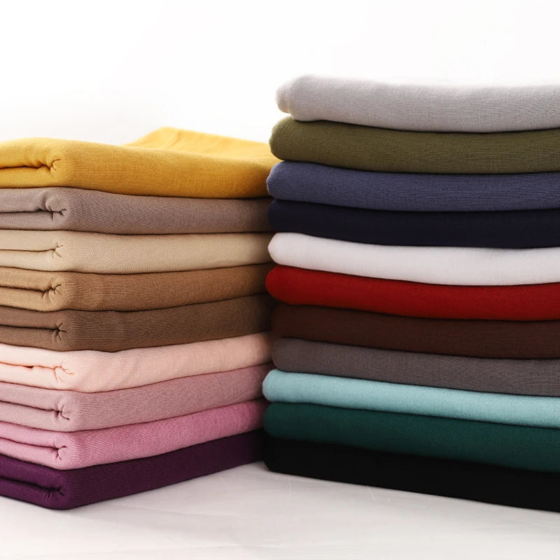 Stapel von 28farbigen Baumwoll-Jersey-Hijab-Schals in verschiedenen Beige-, Braun-, Grau- und dunklen Tönen.