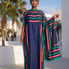 Eine Frau modelliert ein elegantes bedrucktes Seidenkaftankleid mit vertikalen Streifen in blau, rot und grün an einem sonnig