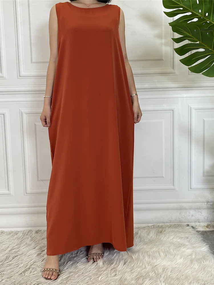 Eine Frau in einem langen, fließenden, ärmellosen, orange-braunen Kaftan steht drinnen.