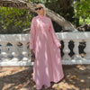 A woman wearing a long pink modest dress and matching headscarf standing outdoors.