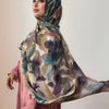 Une femme portant un foulard voile imprimé élégant dans des tons bleu sarcelle, violet et beige.