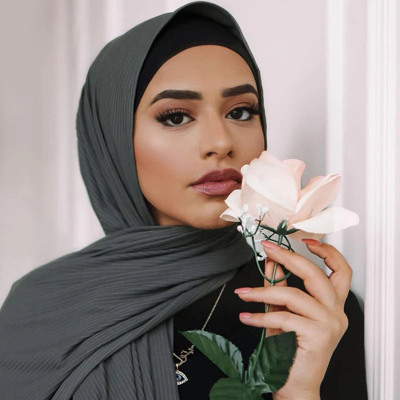 A woman wearing a gray ribbed jersey hijab scarf holding a pink rose.