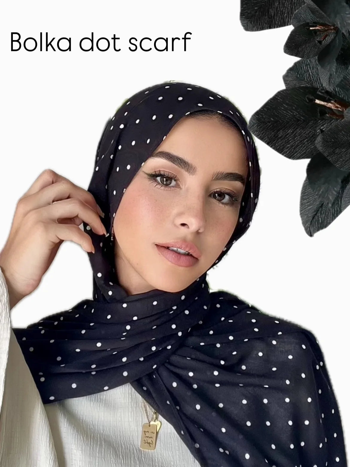 Una mujer vistiendo un hijab de pañuelo de lunares negros con una blusa blanca.