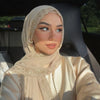 Une femme portant un foulard chiffon beige doux avec un bord en dentelle à cils, regardant l'appareil photo.