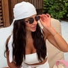 A woman wearing a white silk satin hijab scarf and a white top, posing outdoors.